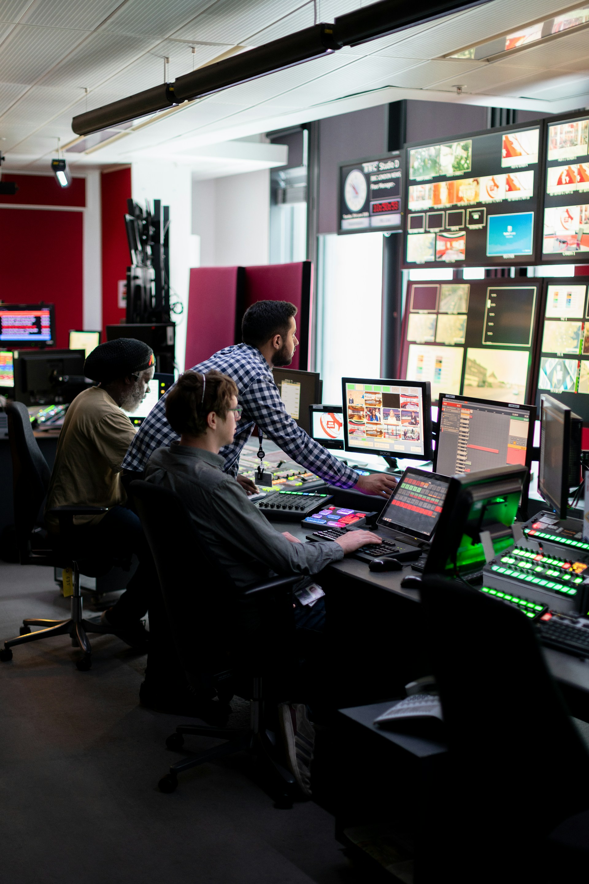 Broadcast engineers monitor studio systems from a control room.