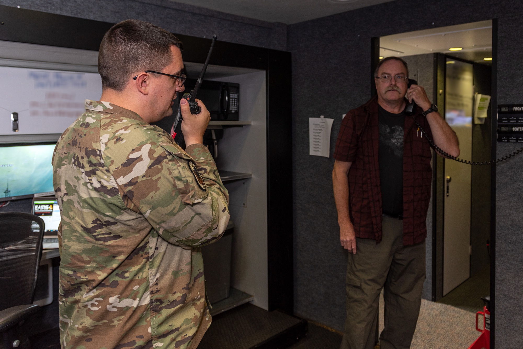 An Air Force emergency management specialist and a civilian communications supervisor test radios inside a mobile operations center.