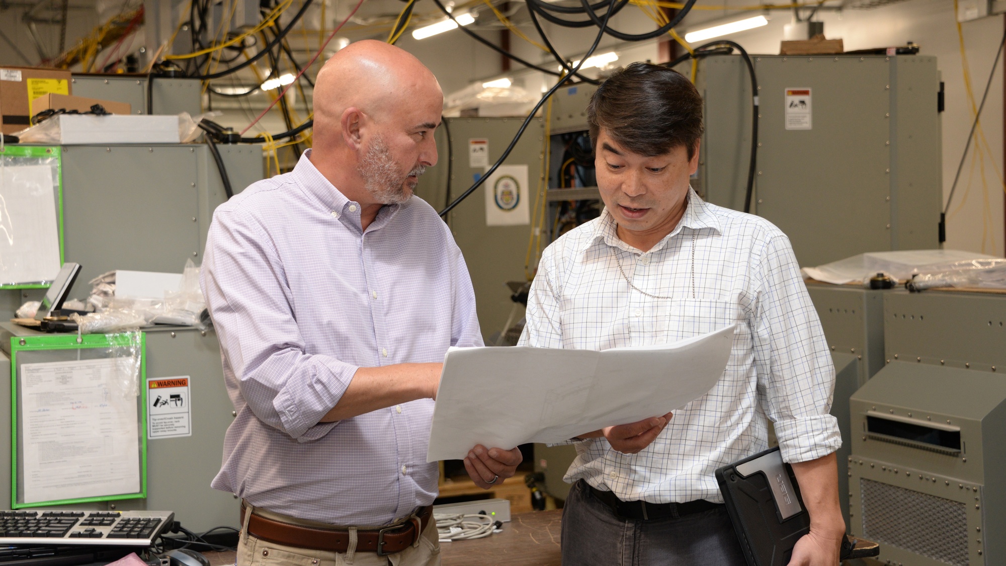 Two Navy network engineering professionals review a rack drawing beside server equipment.