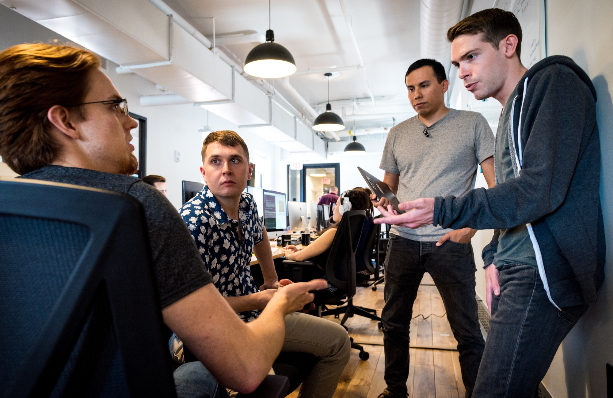 A civilian software engineer and Air Force colleagues in casual clothing discuss a software product beside shared workstations.