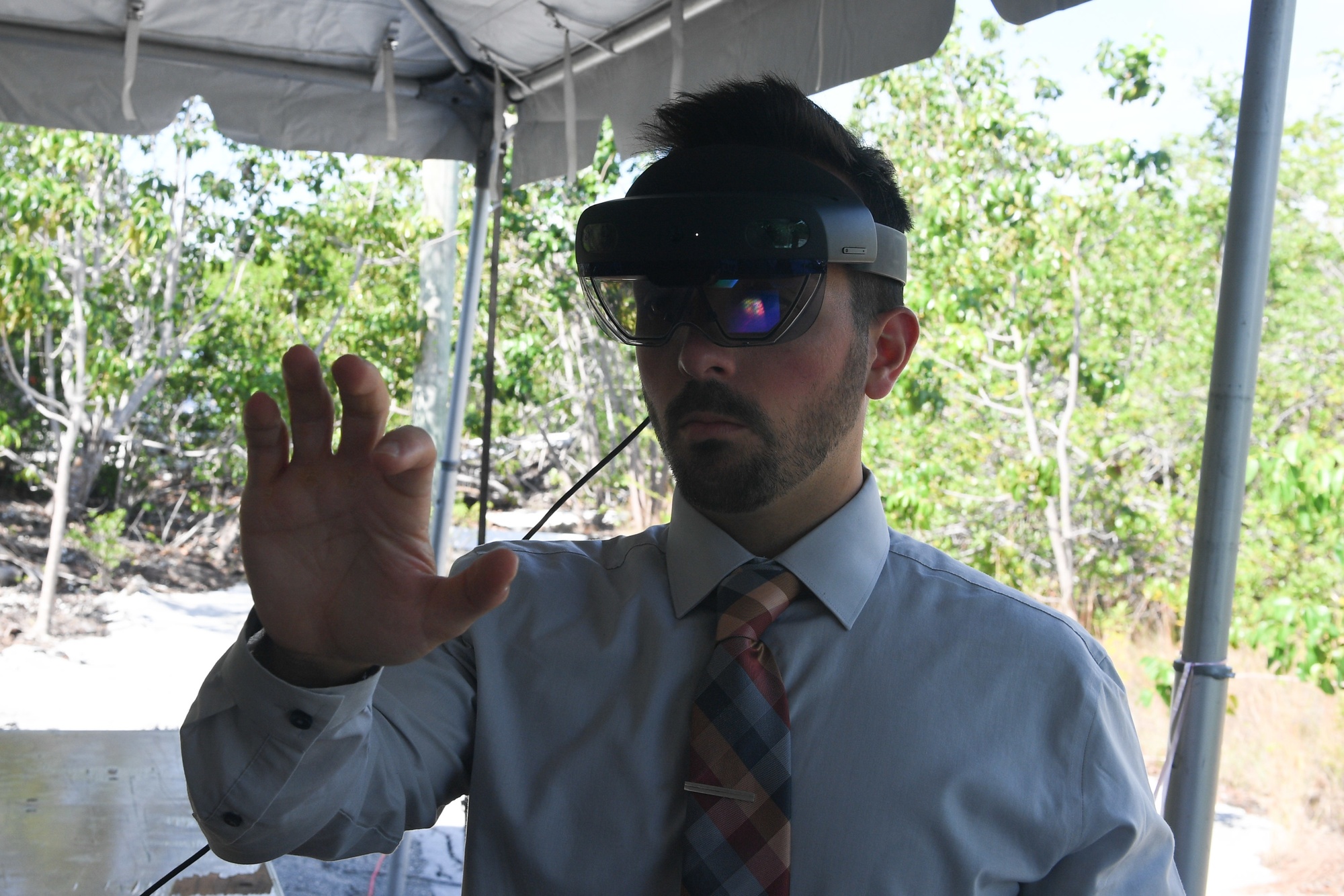 A civilian technology lead demonstrates an augmented-reality headset under a field canopy.